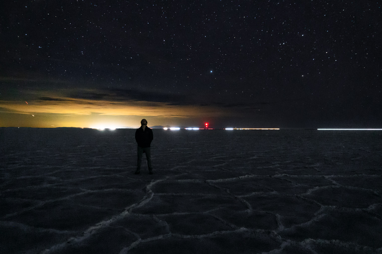 someone looks up at the stars at the salt flats, clouds lit yellow behind